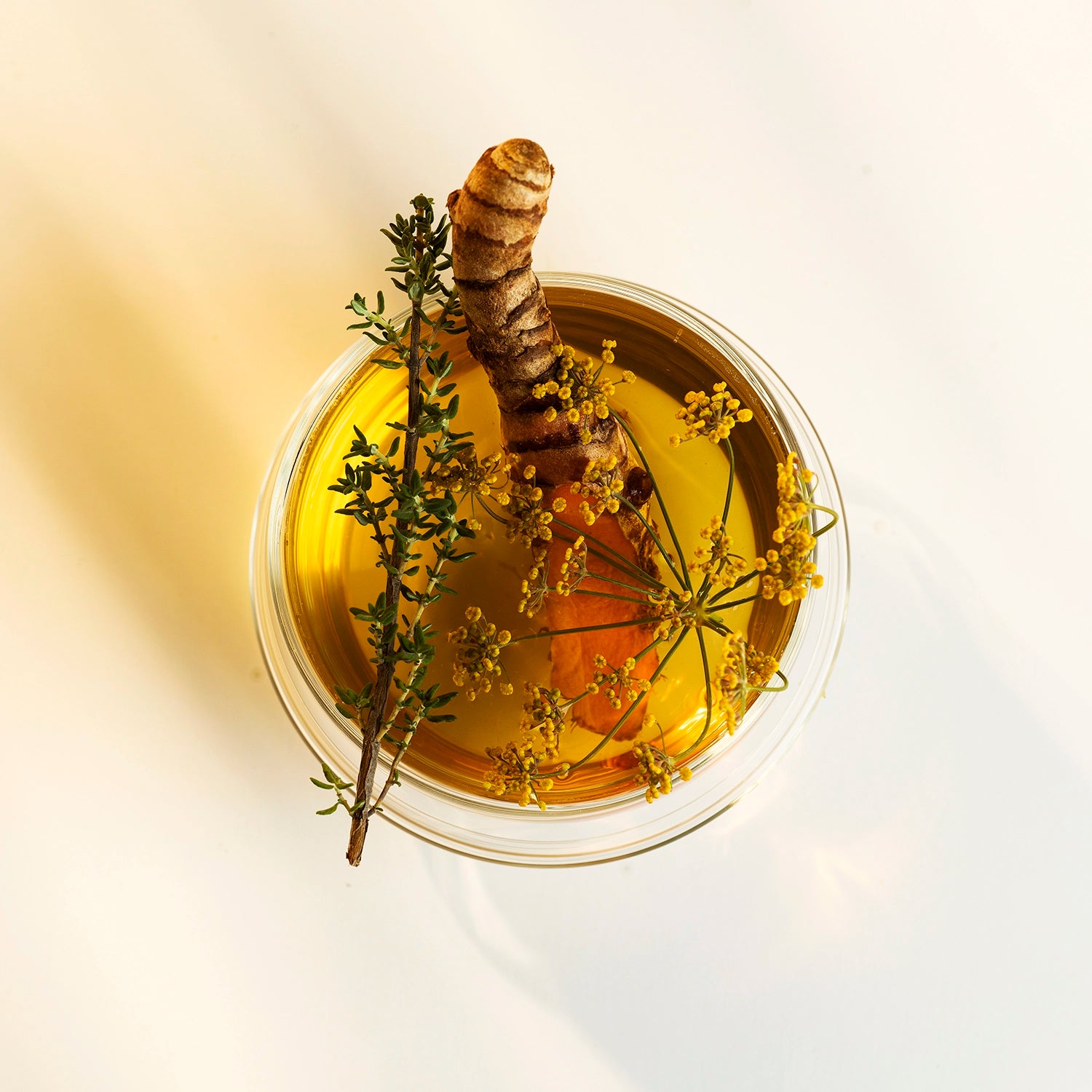 Un liquide jaune dans un verre avec une carotte et des fleurs jaunes.